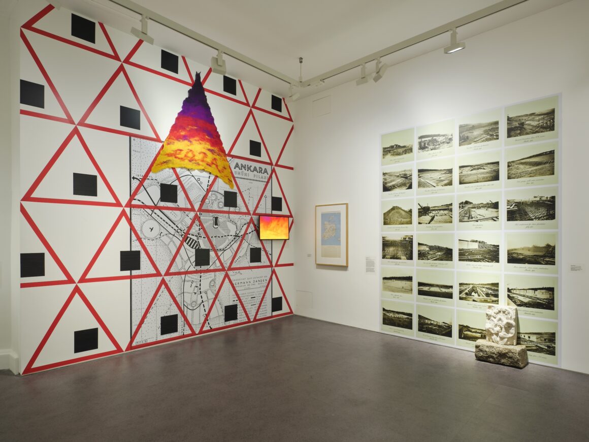 IMMA’s ‘Self-Determination: A Global Perspective’ is a complex, ambitious, and timely exhibition. It draws on how art responded to the seismic political and social changes of 1913 to 1939, when the German, Ottoman, Austro-Hungarian, and Russian empires were reconfigured and when Ireland also gained partial independence. Concentrating on Europe and the near East, as far as Turkey, Palestine and Egypt, it includes work from Ukraine, Poland, Estonia, Latvia, Finland and Ireland, amongst other states and regions. The exhibition prioritises the impact and deployment of the forces of modernity across its themes and structuring. For example, the space devoted to ‘Cross Currents’ encapsulates how the complex networks of empire continued to influence interaction with the wider world. Mary Swanzy’s Samoan Scene (1923), a Gauguin inspired work by the Ukrainian artist, Zola Bielkina, who had not ventured abroad, and Alan Phelan’s sculpture of Roger Casement peering out of an exotic houseplant, share the room with Dragana Jurišić’s 2013 series, ‘YU The Lost Country’, in which the artist revisits the now non-existent Yugoslavia via Rebecca West’s 1941 travelogue. The complex interaction of these works raises questions about how economic and political systems unconsciously impact our worldview. ‘Extractive Industries’ focuses on the construction of hydro-electric schemes in the 1920s and 1930s in Ireland, Poland and Ukraine. Seán Keating’s paintings of Ardnacrusha, familiar to Irish visitors, are contextualised by the work of international artists and by Declan Clarke’s film, and as a result, a more critical reading is apparent. His take on the Siemens project in which Irish workers, especially the Irish speakers, were underpaid and mistreated is alluded to in the minutiae of their onsite living conditions. Dnieper Dam (1932) by Dmytro Vlasiuk depicts the imposition of this gigantic modernist structure into the pastoral setting of Ukraine. The dam was part of the expansion of the Soviet Union, then in control of the region. Concentrating on agricultural workers, the painting alludes to the ways in which the industrial scheme caused the flooding of acres of farmland and the displacement of rural land dwellers. A neighbouring dam at Kherson Oblast made headlines in June 2023 when it was blown up by the Russian Army as part of its campaign to retake Ukrainian territory. Rafał Malczewski’s Building of the Roznow Dam (1938) refers to the development of an industrial infrastructure of the Second Polish Republic, founded in 1918. The bright mountainous landscape is latticed off by wires and the geometric constructions of the dam, in a work which accentuates aesthetics over politics. In the Garden Galleries, the theme moves from a state perspective to that of the citizen, including those marginalised by new regimes. Aesthetics seem more to the fore or perhaps this reflects the move away from official ideologies. The impressive pairing of William Conor’s cartoon for the mural, Ulster Past and Present (c. 1931) with Kristjan Raud, City Under Construction (1935) refers to how the ruins of the past were revisited to create national mythologies. Conor connects ancient Ulster warriors with the factory and shipyard workers of the new Northern Ireland, while Raud’s work alludes to the Estonian national epic, Kalevipoeg (1857). This folktale, like those of Ireland, equates the construction of ancient tombs and landmarks with the heroic deeds of the past and provides a sense of pride in the nation’s ancient prowess for its modern citizens. The basement of the Garden Galleries is given over to the delightfully irreverent ‘Reconciliations’, presided over by Phelan’s De Valera with his tongue out. Here, dances and social gatherings of all kinds and in all styles bring in the carnivalesque, perhaps most evident in the juxtaposing of two of William Orpen’s depictions of celebrations of Armistice Day in Arras with the bizarre Village Wedding (1926) by the Slovenian painter, Tone Kralj. The drunken antics of Orpen’s traumatised celebrants contrast wonderfully with the metallic embracing peasants of Krajl’s nuptial festivities. In both the war casts its shadow. Krajl’s deployment of modernist forms, ultimately derived from cubism, is echoed throughout the exhibition in works by artists who lived in Paris or who learnt about it second hand. Several artists including Mainie Jellett and Evie Hone studied there with André Lhote, and there are some startling comparisons to be made with other regions here, such as the works of the Serbian artist, Sava Šumanović, another former Lhotean, who was executed in 1942 after the establishment of the pro-Nazi Croatian state in Serbia. Many of the paintings by the Ukrainian artists were banned under Stalin in the 1930s and were only allowed to be displayed after Ukraine achieved independence in 1991. Now these works are again in storage, except for those in this exhibition. Contemporary artworks provide a crucial element of reflection and disruption to what might otherwise be a pedestrian art historical display. Minna Henriksson’s wall drawing, Limits of the State (2023), traces the comparative experience of women in Ireland and Finland in the aftermath of independence, when in both cases, their role was defined in terms of home and family. This freehand, transient plotting of legislation could be seen as a metaphor for the entire exhibition, revealing how fragmented and arbitrary the division of power is, and how necessary research and uncovering of facts has become in our relationship to our national and global histories. The playful works of Ursula Burke, Alan Phelan and Array Collective punctuate the monumentality of much of the older works and bring in contemporary skepticism towards official histories and national myths. Sasha Sykes’s Trove III (2023), an ivy, wood and hessian construction of an imagined ruined chimneypiece, a relic of the Ascendancy House, is a reminder of the vagaries of history to which we are all subject. Larissa Sansour’s film, Familiar Phantoms (2023) creates a narrative of her family’s complex history of displacement and enduring trauma of exile from Palestine. Jasmina Cibic’s Beacons (2023), a film set in a series of isolated buildings, re-uses the rhetoric of transnationalism to consider the position of women and the soft power of architecture. Situated at the end of the exhibition in the main building, it is perhaps an opening to the wider repercussions of self-determination in the era of globalisation. This is a stimulating and challenging exhibition, its theme more relevant now than ever. It makes a case for the need to look beyond the borders of our own state and to situate ourselves within a broader constantly evolving history. ‘Self-Determination’ asserts art’s role in imagining the nation but equally reminds us that its task is also to critique the boundaries of the state and its often-rudimentary ideologies. Dr Róisín Kennedy lectures in the School of Art History and Cultural Policy at UCD.